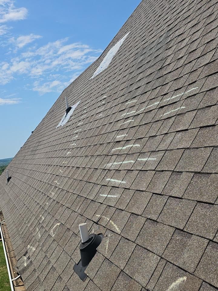 Steep shingled roof with a small vent and skylight under a blue, partly cloudy sky