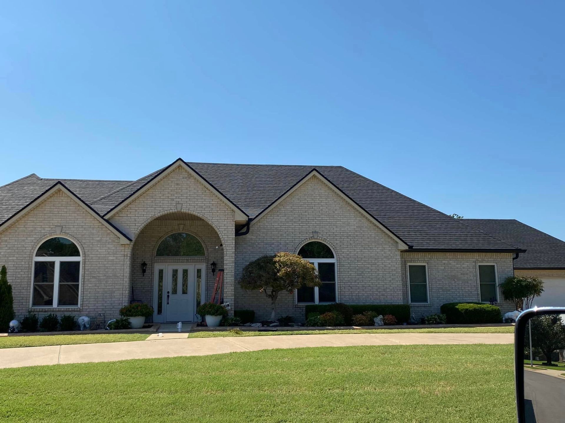 Single-story suburban house with arched windows, stone facade, and a manicured lawn under a clear blue sky