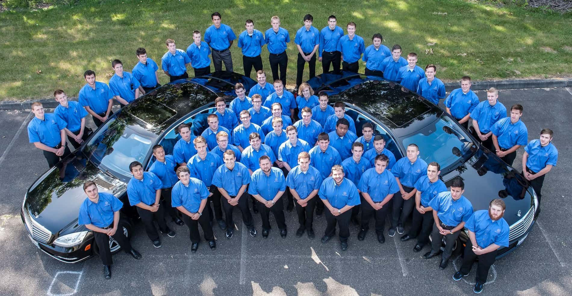 People in blue shirts posing around a black car in a parking lot