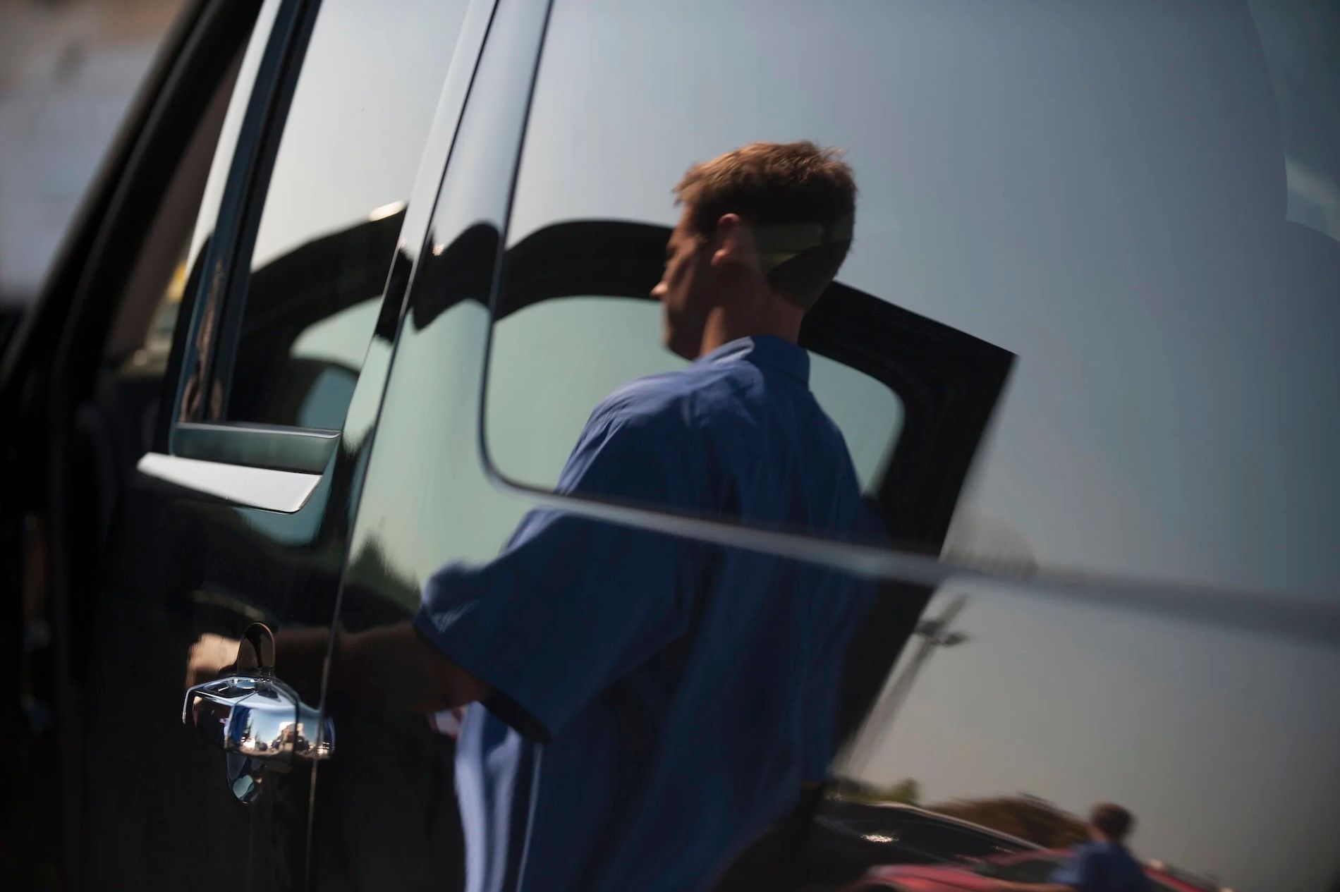 Person in blue shirt standing by a car door, seen through the open window.