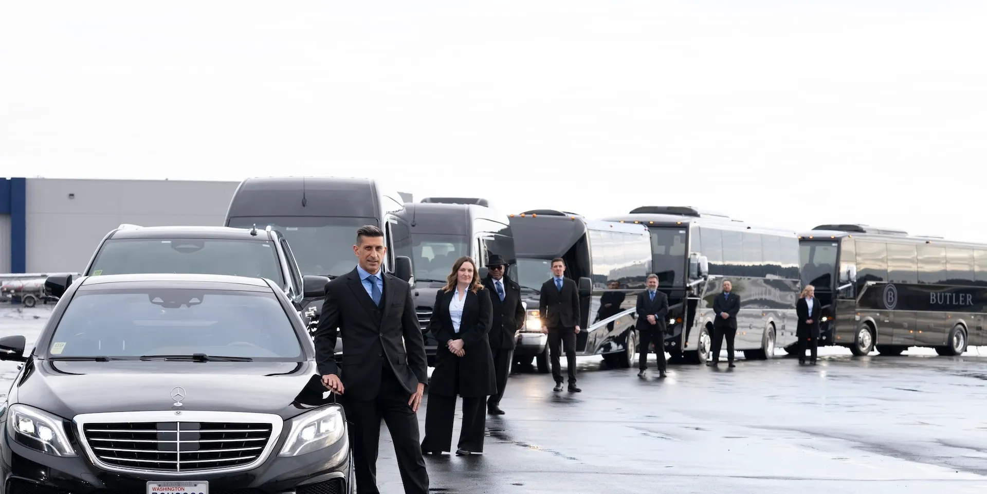 Black vehicles and several people on a wet tarmac beside a large private jet, with one man walking forward