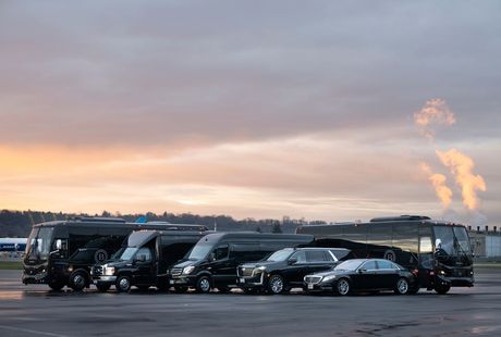 Line of black cars and vans parked on an airport tarmac at sunset, with steam rising in the background