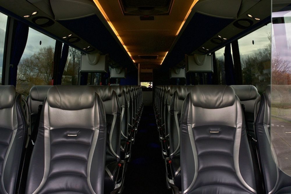 Empty luxury bus interior with black leather seats and warm ceiling lights.
