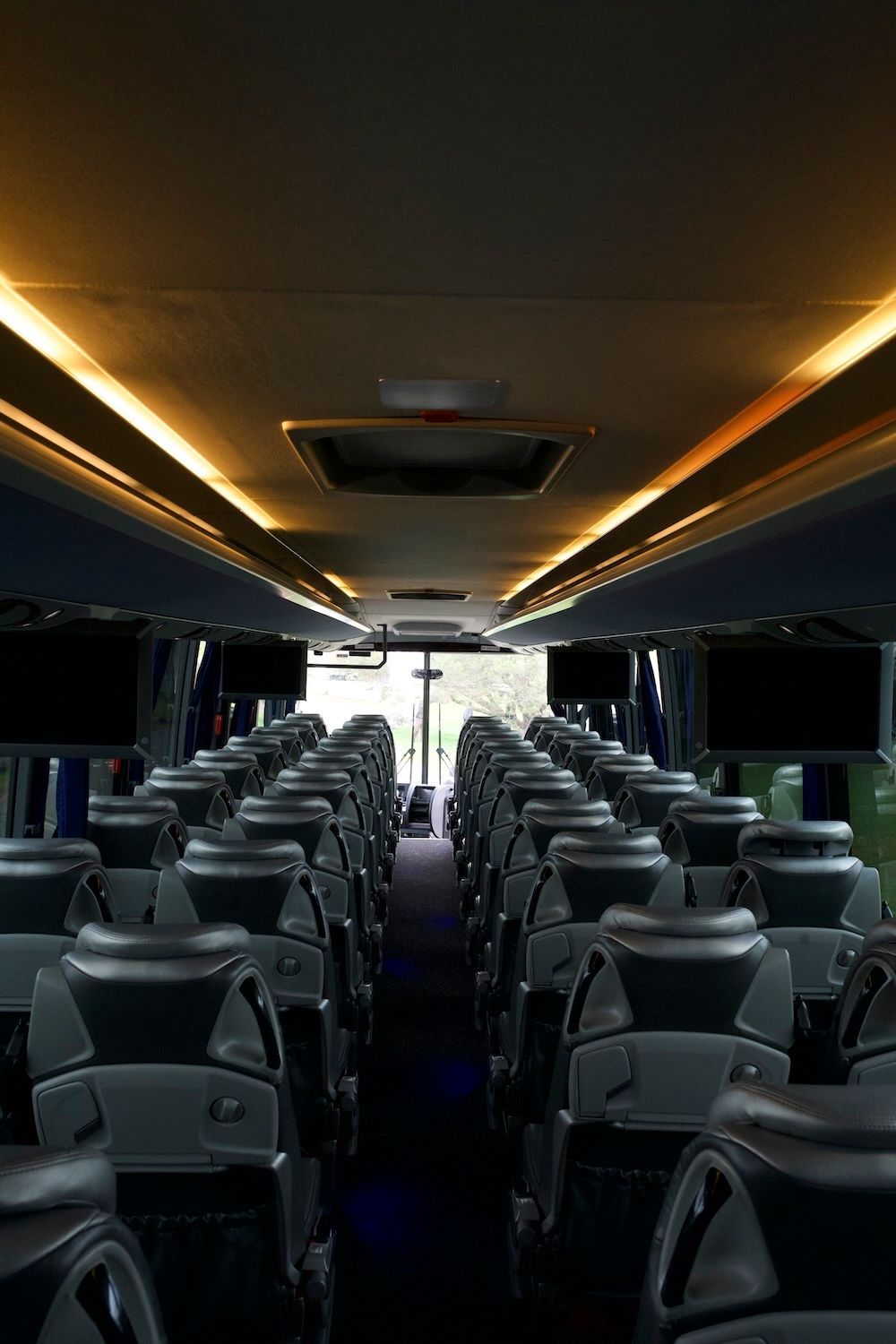 Empty luxury coach bus interior with rows of dark seats and warm ceiling lights