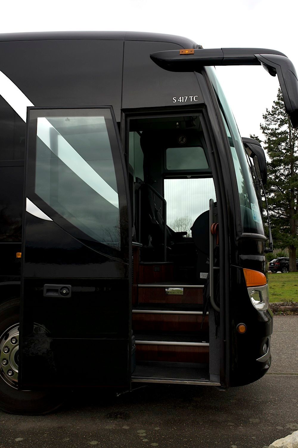 Black coach bus with open door and extended wheelchair lift at the curb.