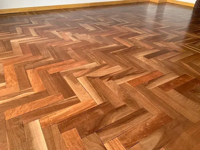 Habitación vacía con suelo de madera brillante en espiga y paredes amarillas.