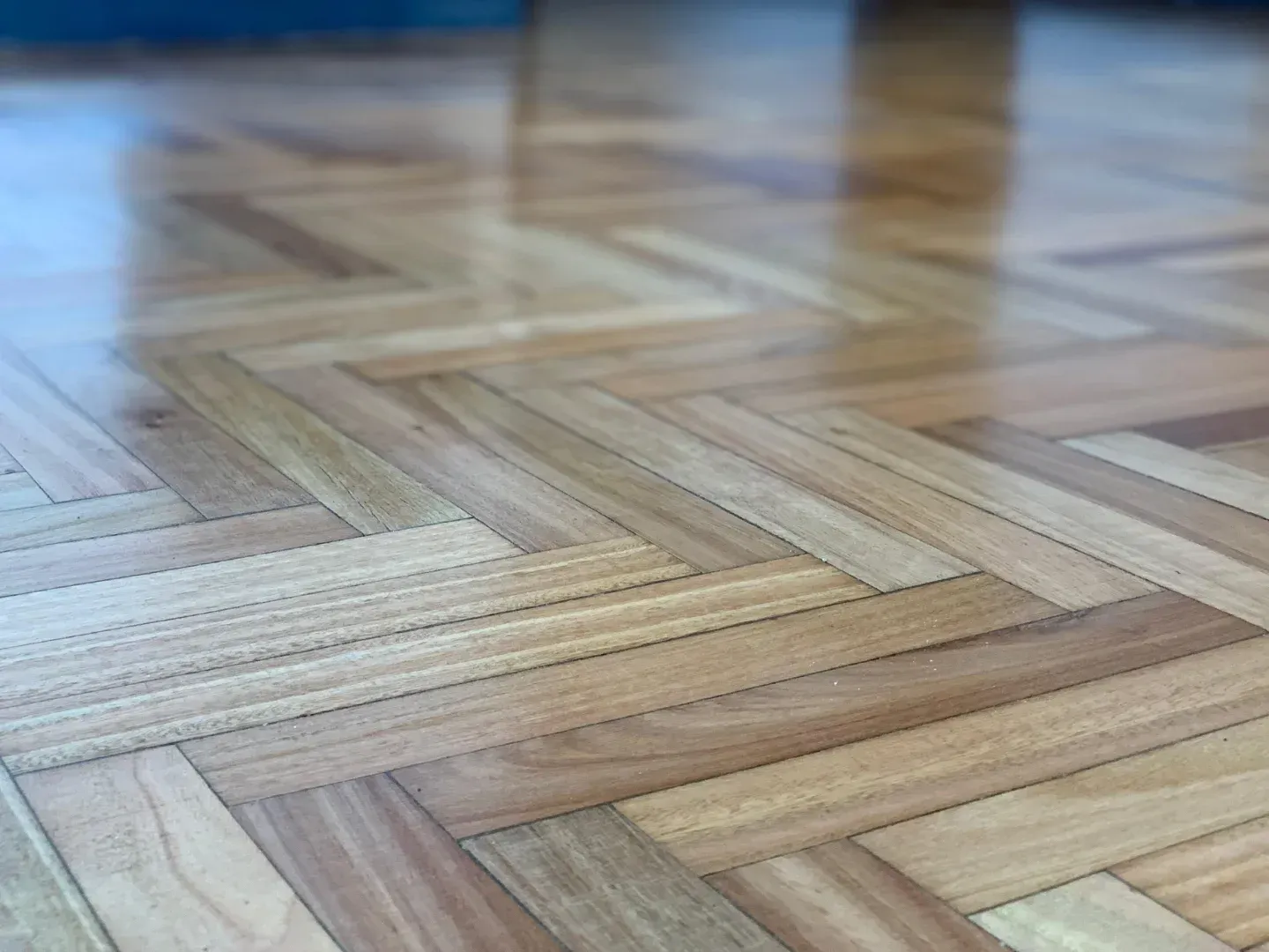 Primer plano de un suelo de madera clara con diseño de espiga y una pared azul al fondo.
