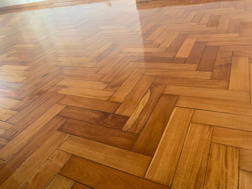 Suelo de madera en espiga bañado por el sol, con cálidos tonos marrones y reflejos.
