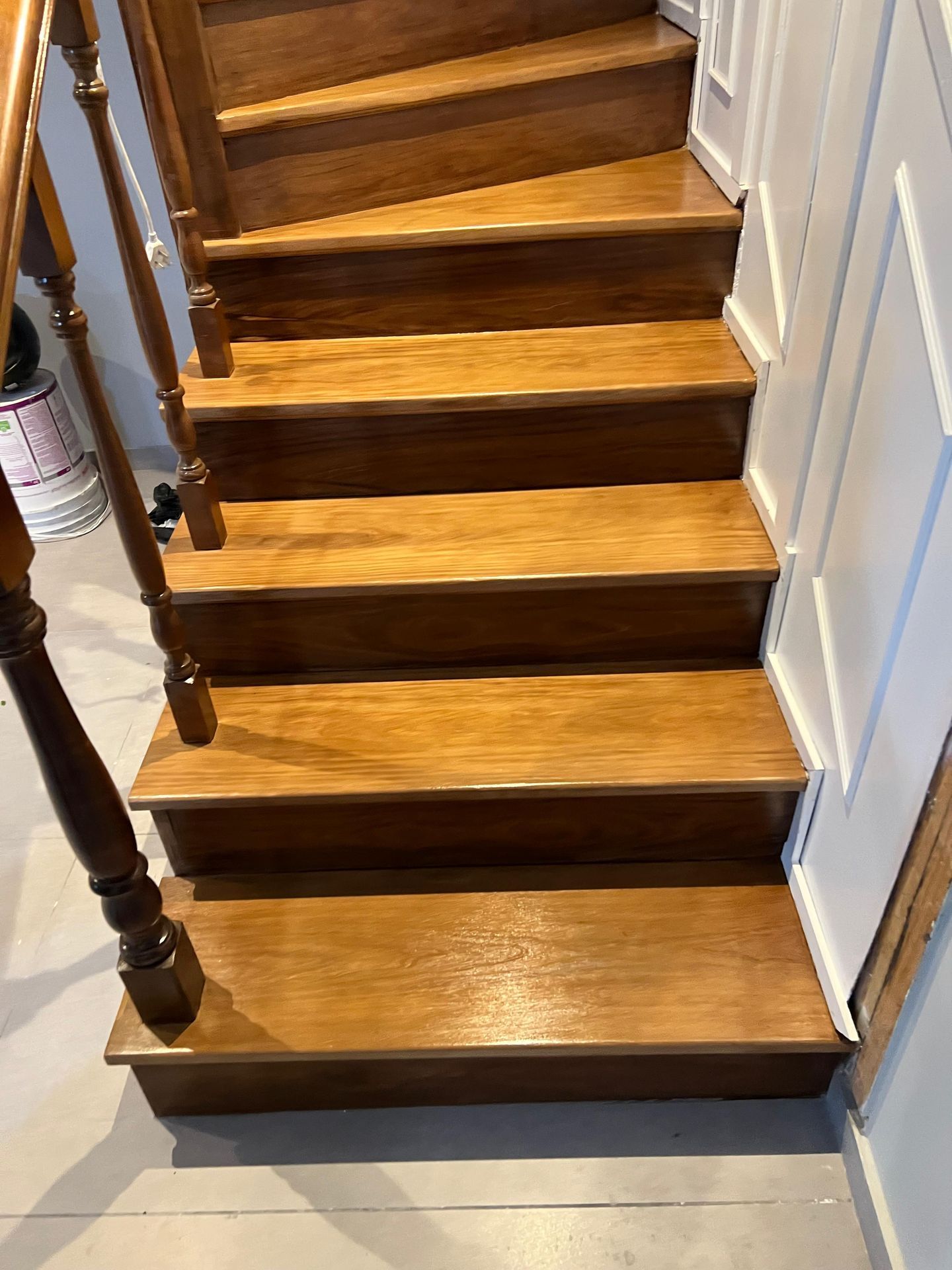 Escalera de madera con peldaños oscuros, contrahuellas blancas y pasamanos junto a una pared blanca.