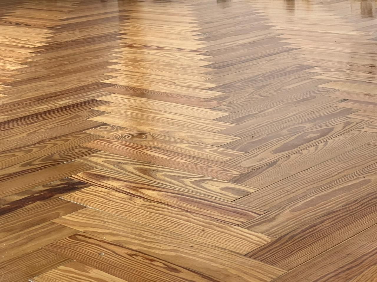 Primer plano de un suelo de madera en espiga con tonos marrones cálidos y acabado brillante.
