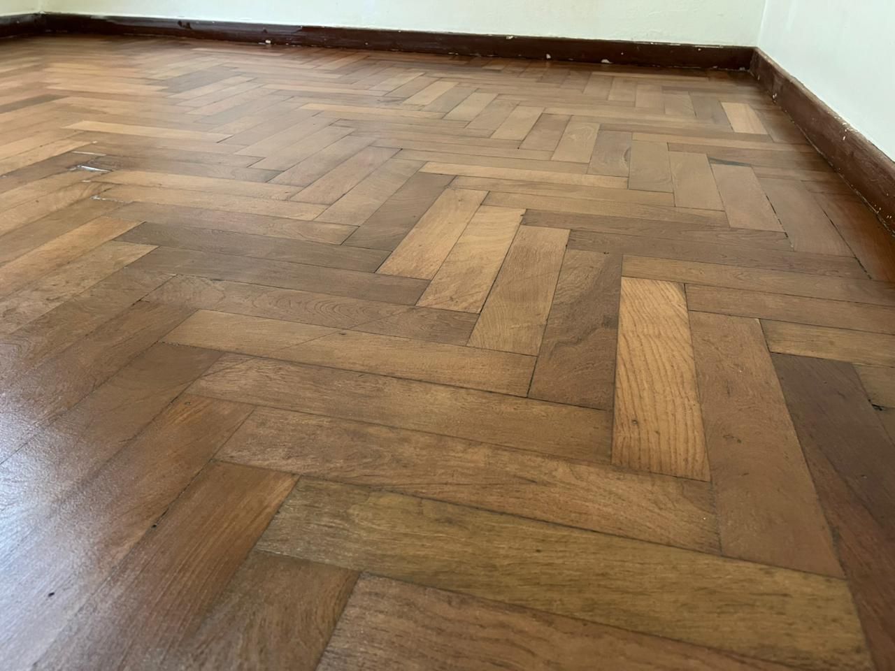 Habitación vacía con suelo de madera en espiga y paredes blancas.