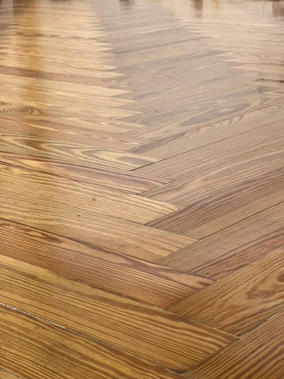 Primer plano de un suelo de madera brillante con diseño de espiga en tonos marrones cálidos.