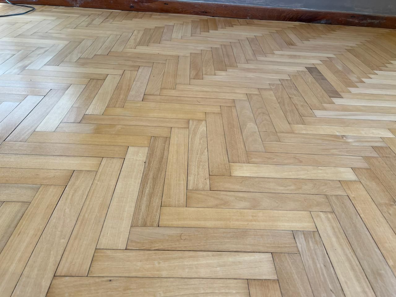 Suelo de parquet de madera con diseño de espiga y acabado natural claro.