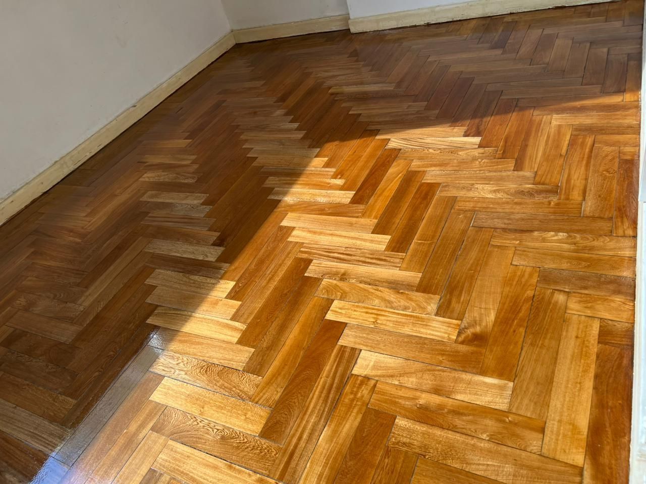 Suelo de parquet de espiga bañado por el sol con una sección dañada cerca de la pared.