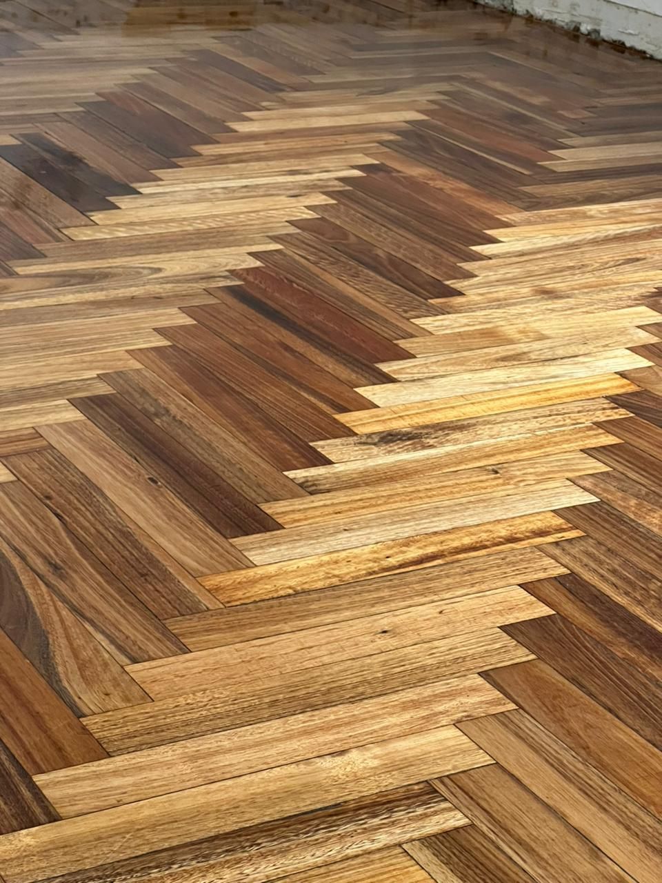 Primer plano de un suelo de madera en espiga con tablones claros y oscuros alternados en un patrón en zigzag.