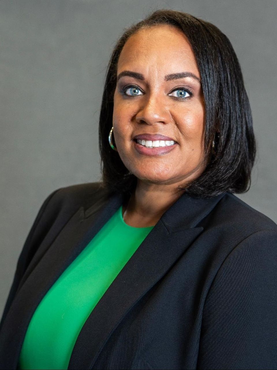 a woman wearing a green shirt and a black jacket is smiling for the camera .