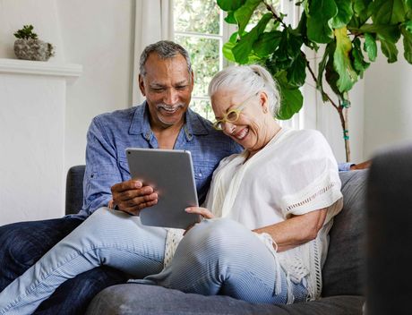 a man and a woman are sitting on a couch looking at a tablet