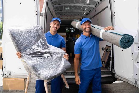 two movers are holding a chair and a rug in front of a van