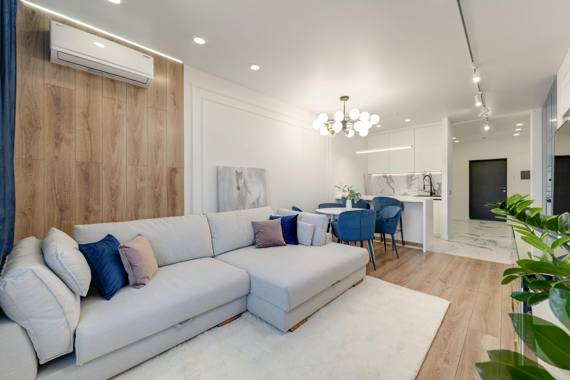 Modern living room with light-colored sofa, wood panel wall, and open kitchen with dining area.