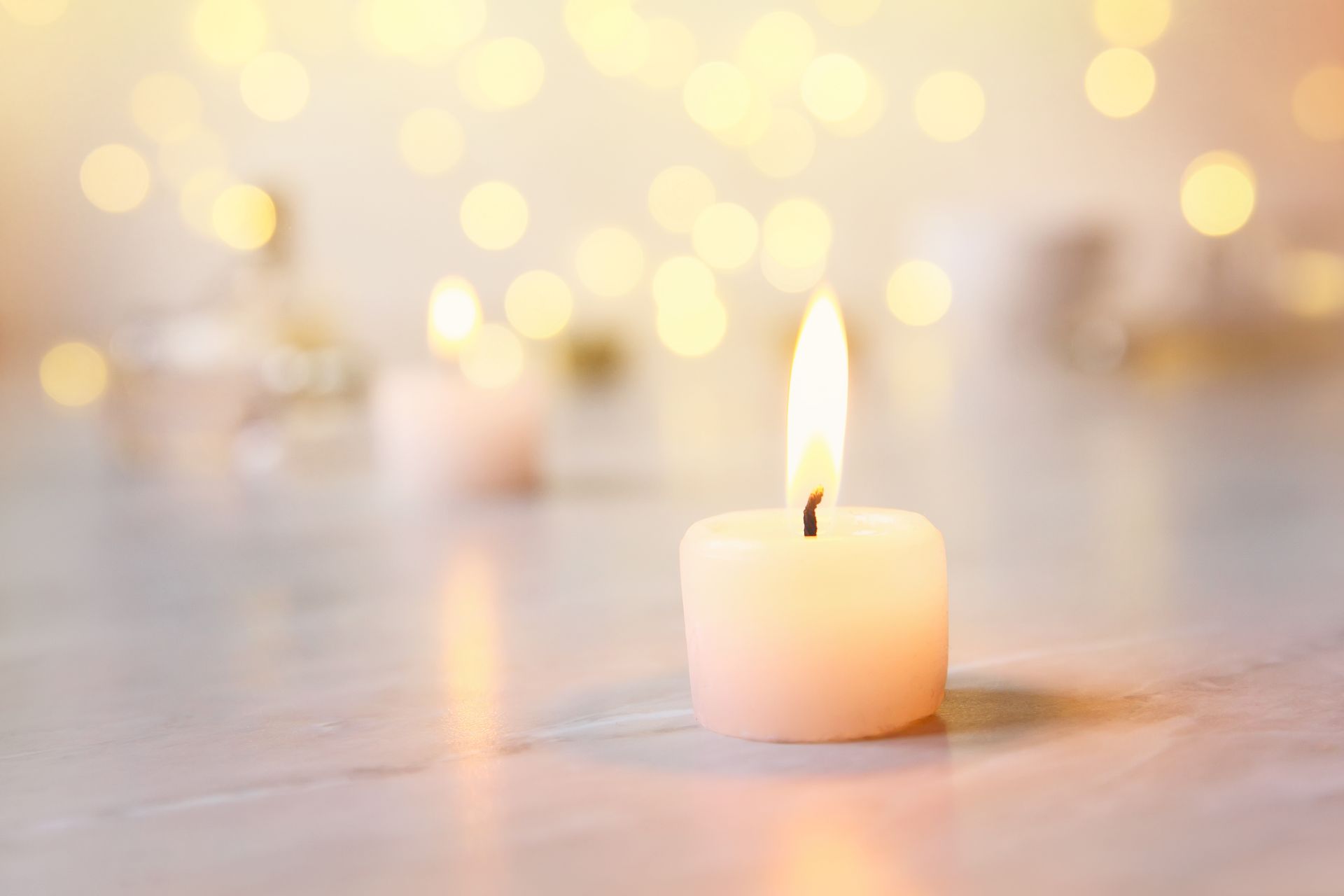Small lit white candle on a soft, blurred background with warm golden lights