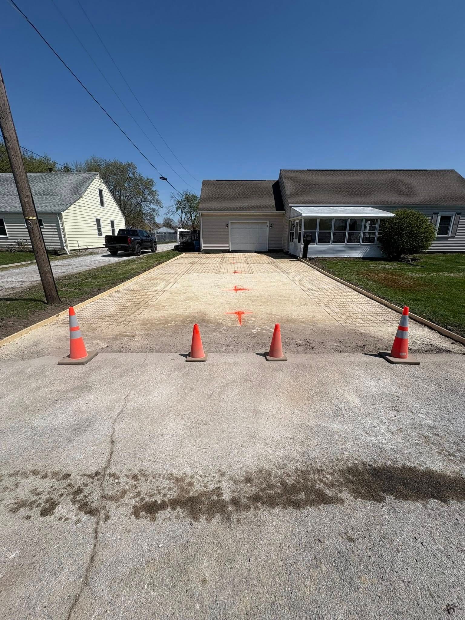 A gravel driveway leading to a house, marked with orange traffic cones and stakes, under a clear blue sky.