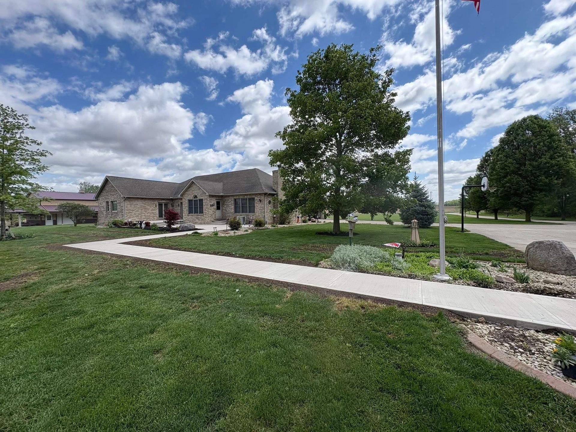 A concrete walkway leads through a grassy lawn toward a stone building under a blue sky with fluffy white clouds.