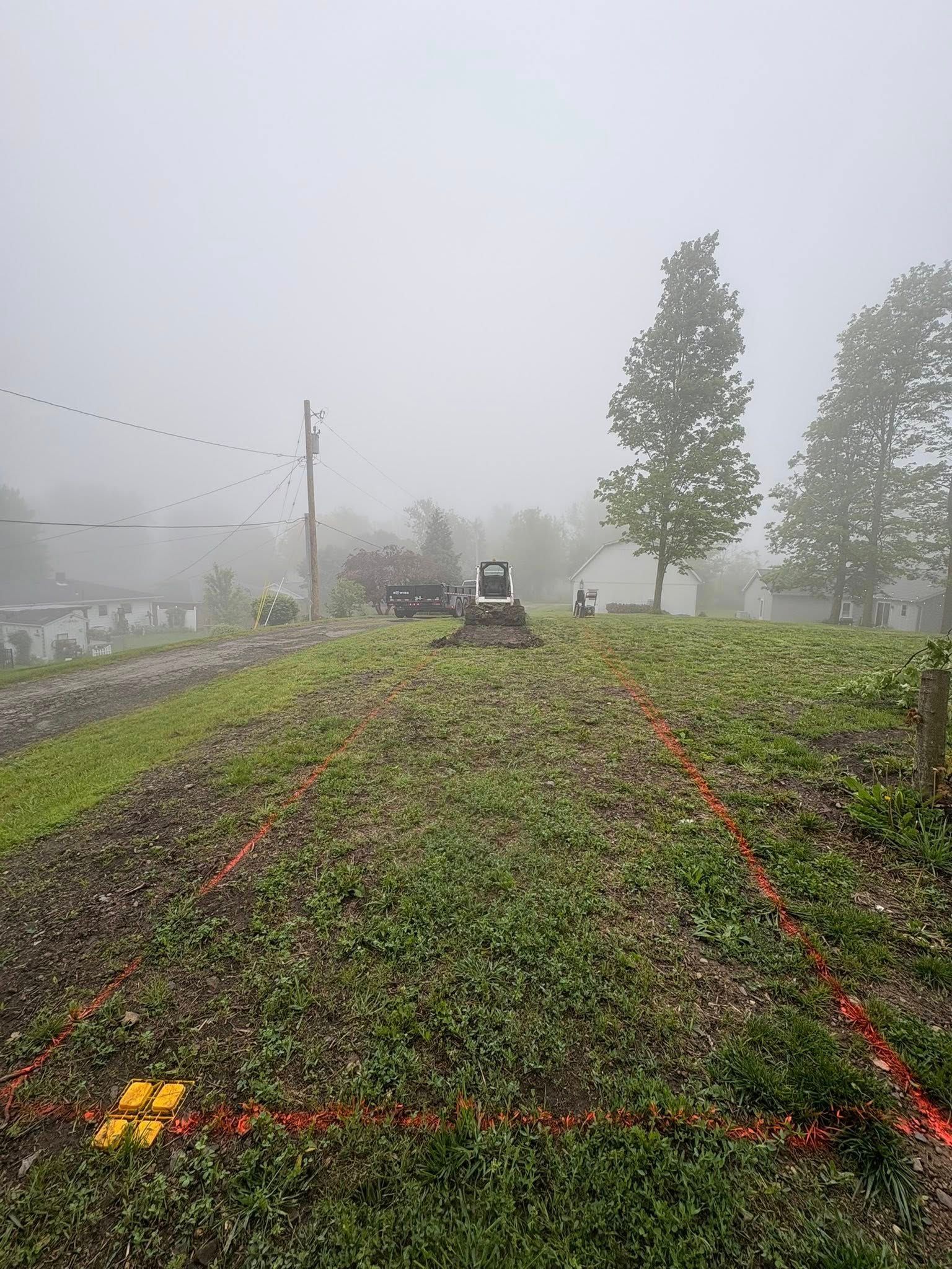 A construction site on a foggy day, with red spray-painted markers outlining a rectangle in a field near heavy equipment.