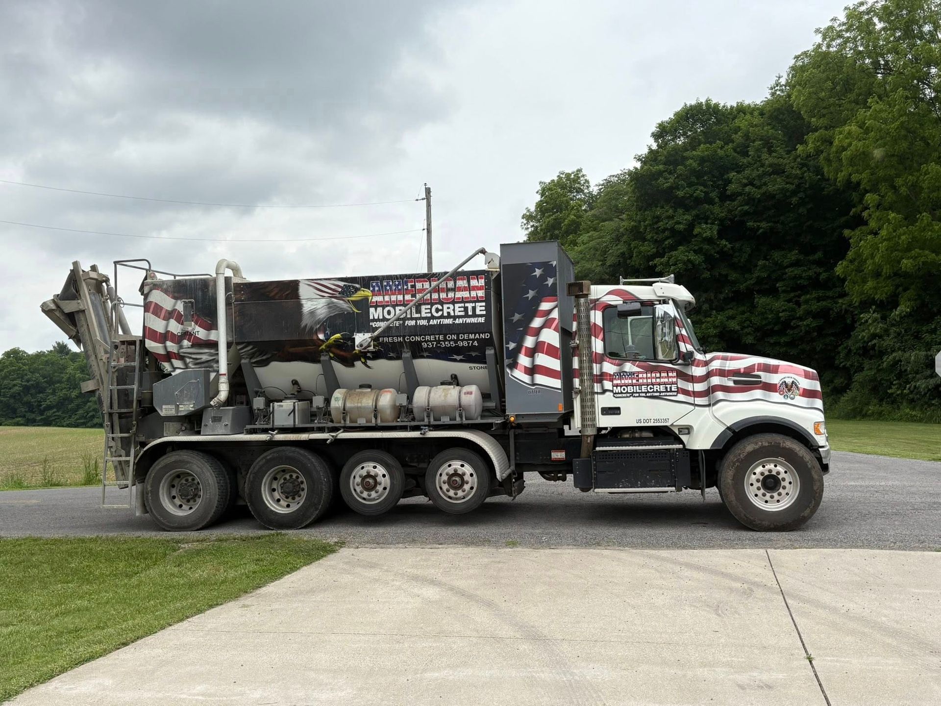 A side view of a commercial truck with an American flag paint scheme, parked on a road beside a grassy field.
