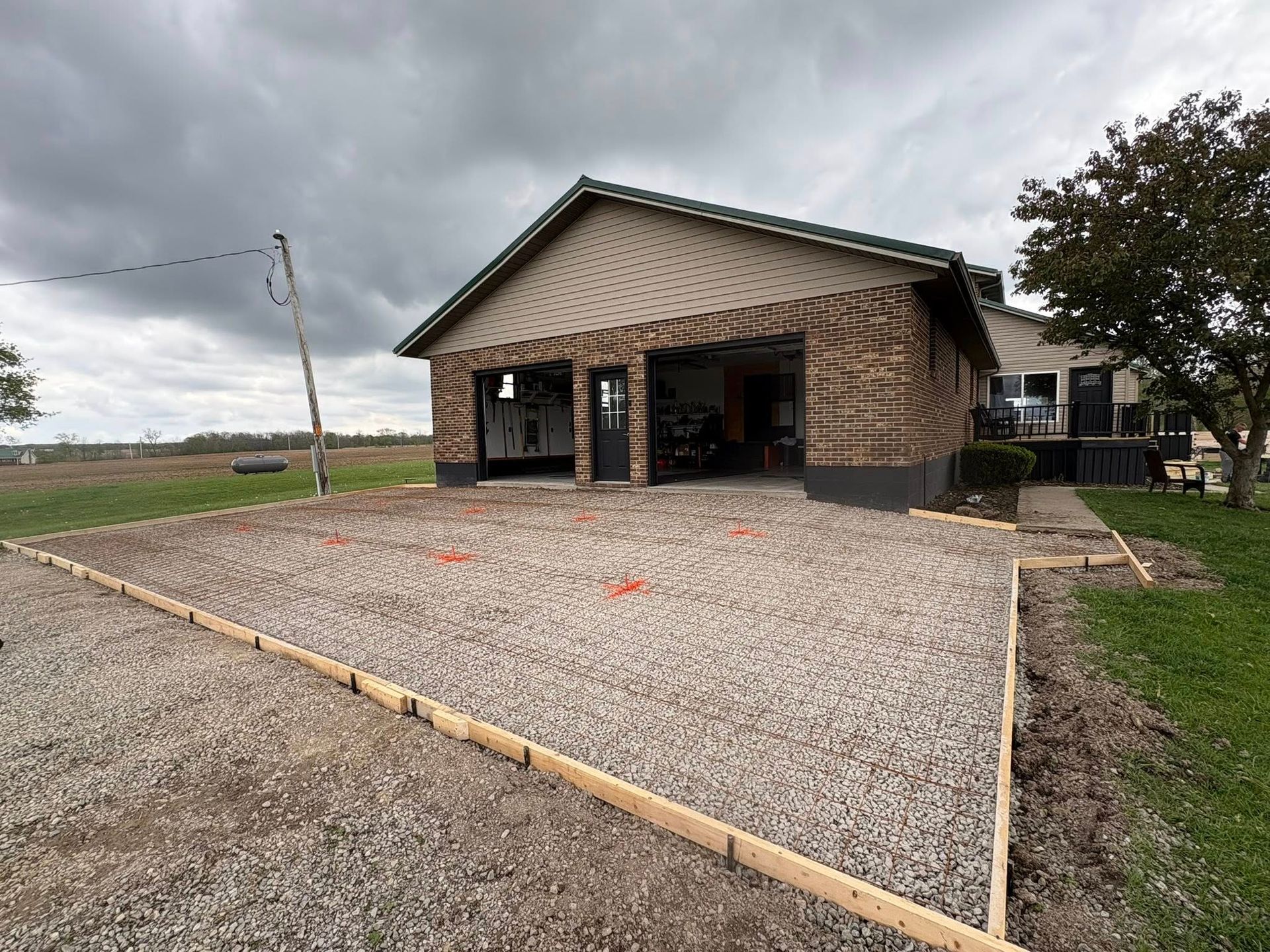 A gravel area with wooden framing borders, prepared in front of a two-car garage at a brick and siding home.