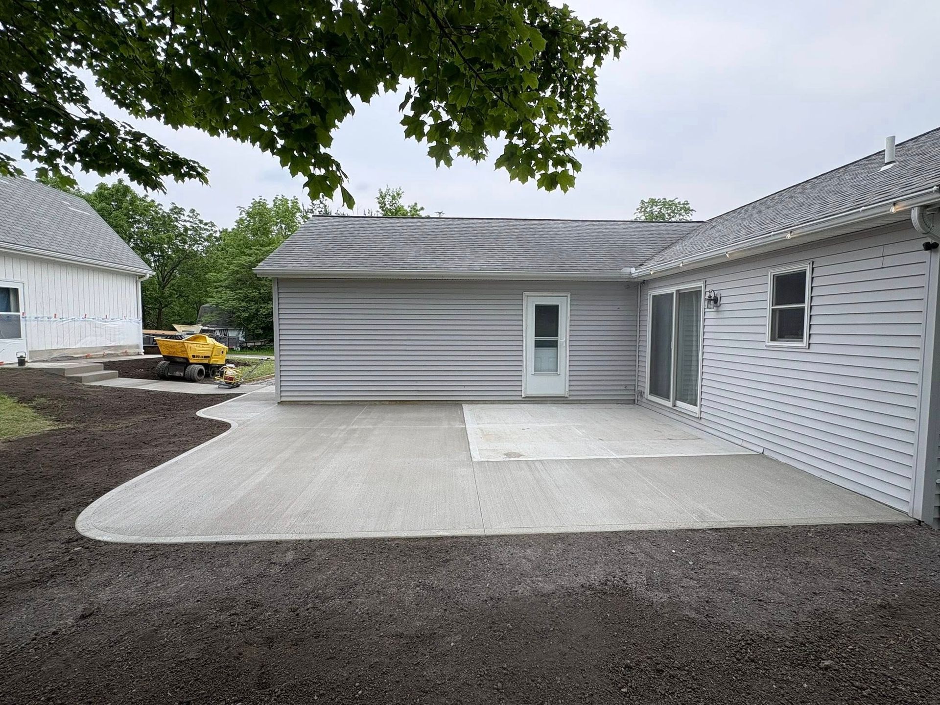 A newly poured light gray concrete patio sits against the side of a house with light gray siding and a white door.