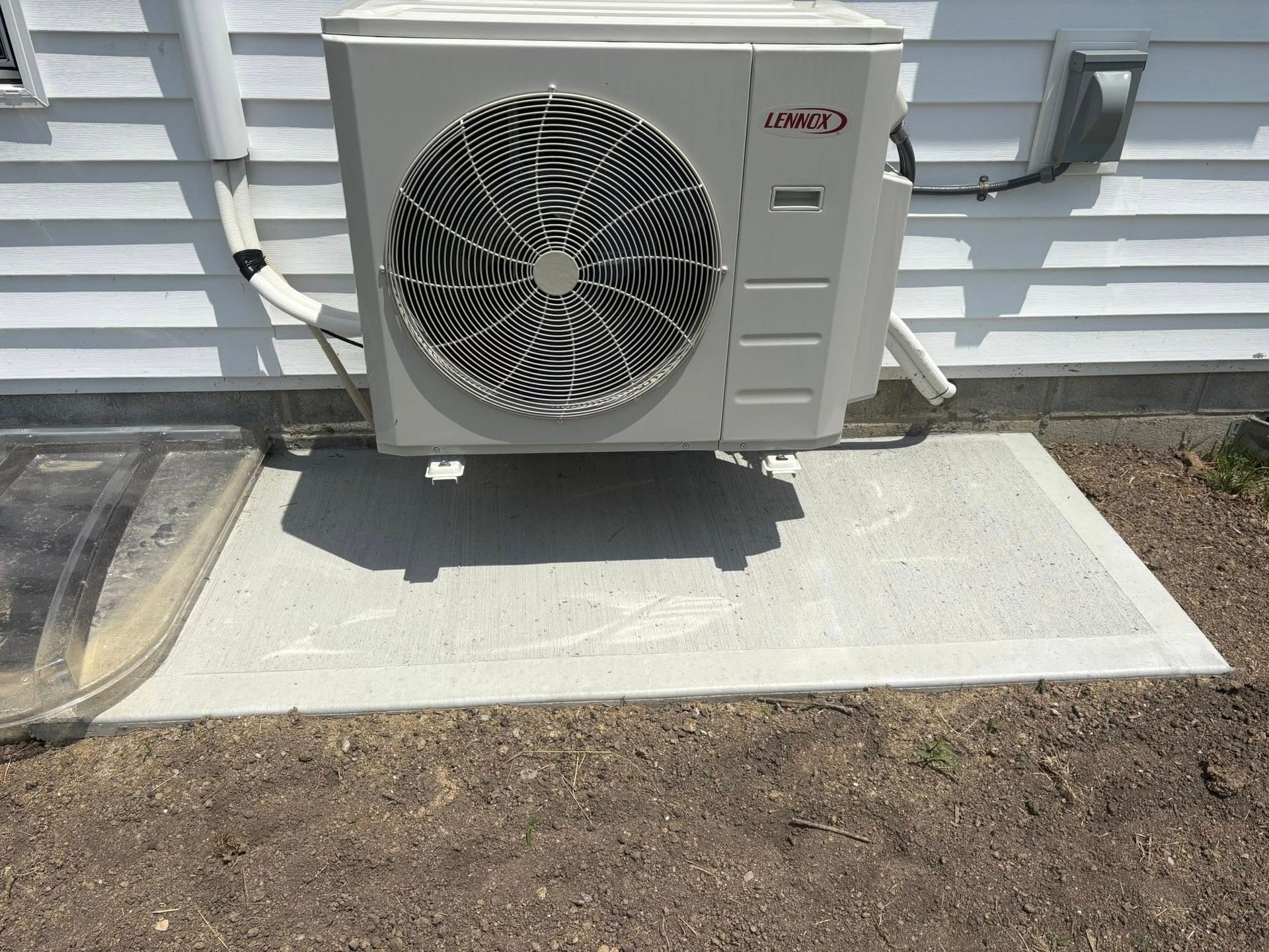 A grey outdoor HVAC unit mounted on a wall bracket above a flat concrete pad against white horizontal siding.