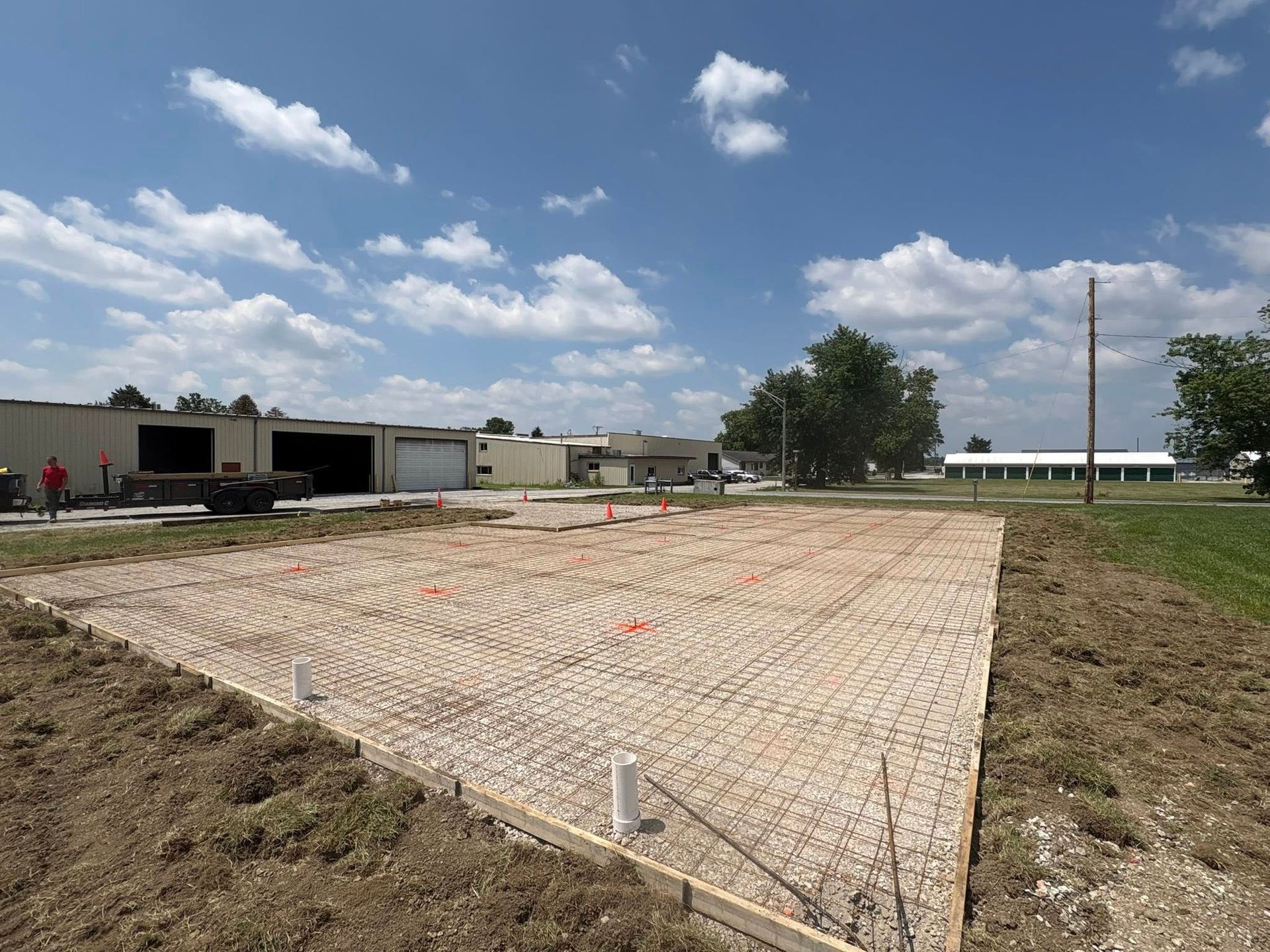 A rectangular construction site with wire mesh and plumbing pipes prepared for a concrete slab foundation.