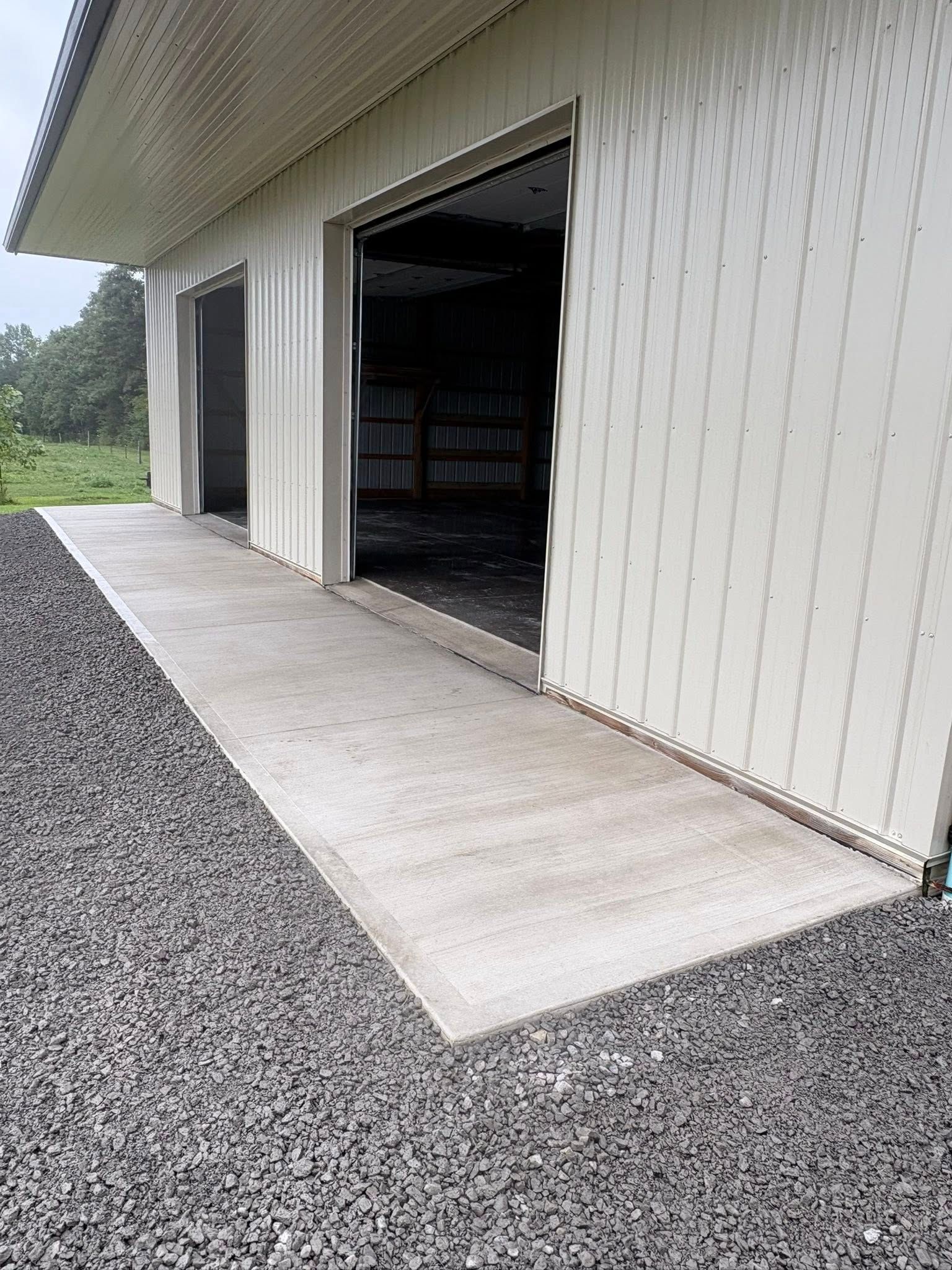A cream-colored metal building with large open doorways leading to a concrete walkway surrounded by gray gravel.