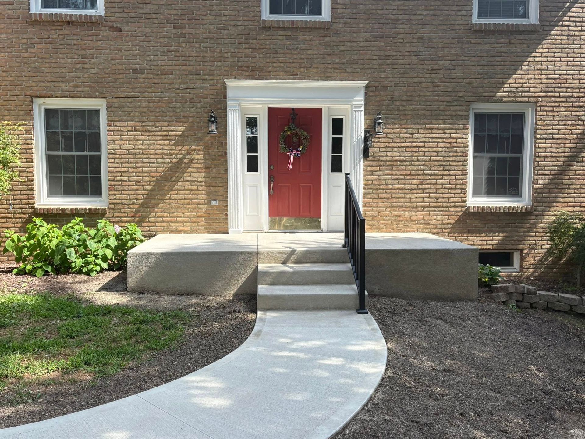 A brick house with a red front door, a white entry frame, three front steps, and a curved concrete walkway.