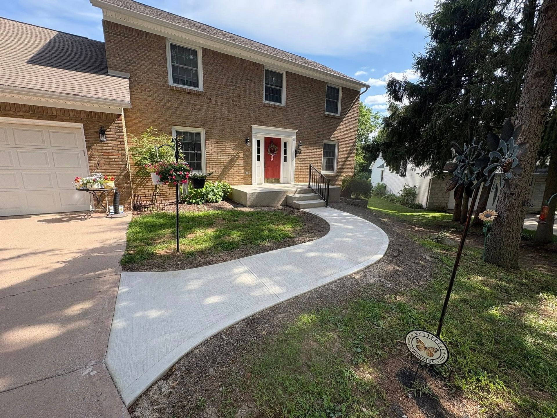 A two-story brick house with a white front door and a newly paved concrete walkway leading to the entrance.