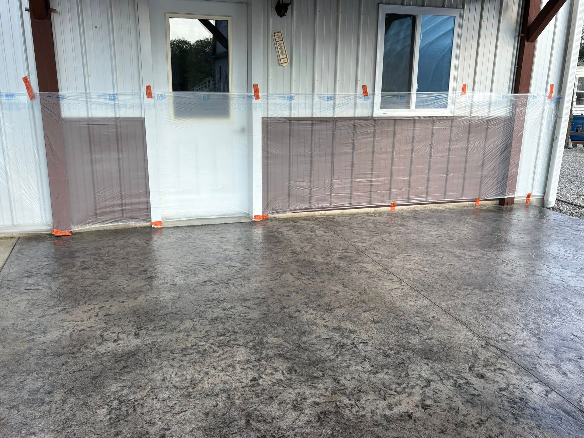 A newly poured concrete patio with a decorative stamped texture in front of a white building with a door and window.