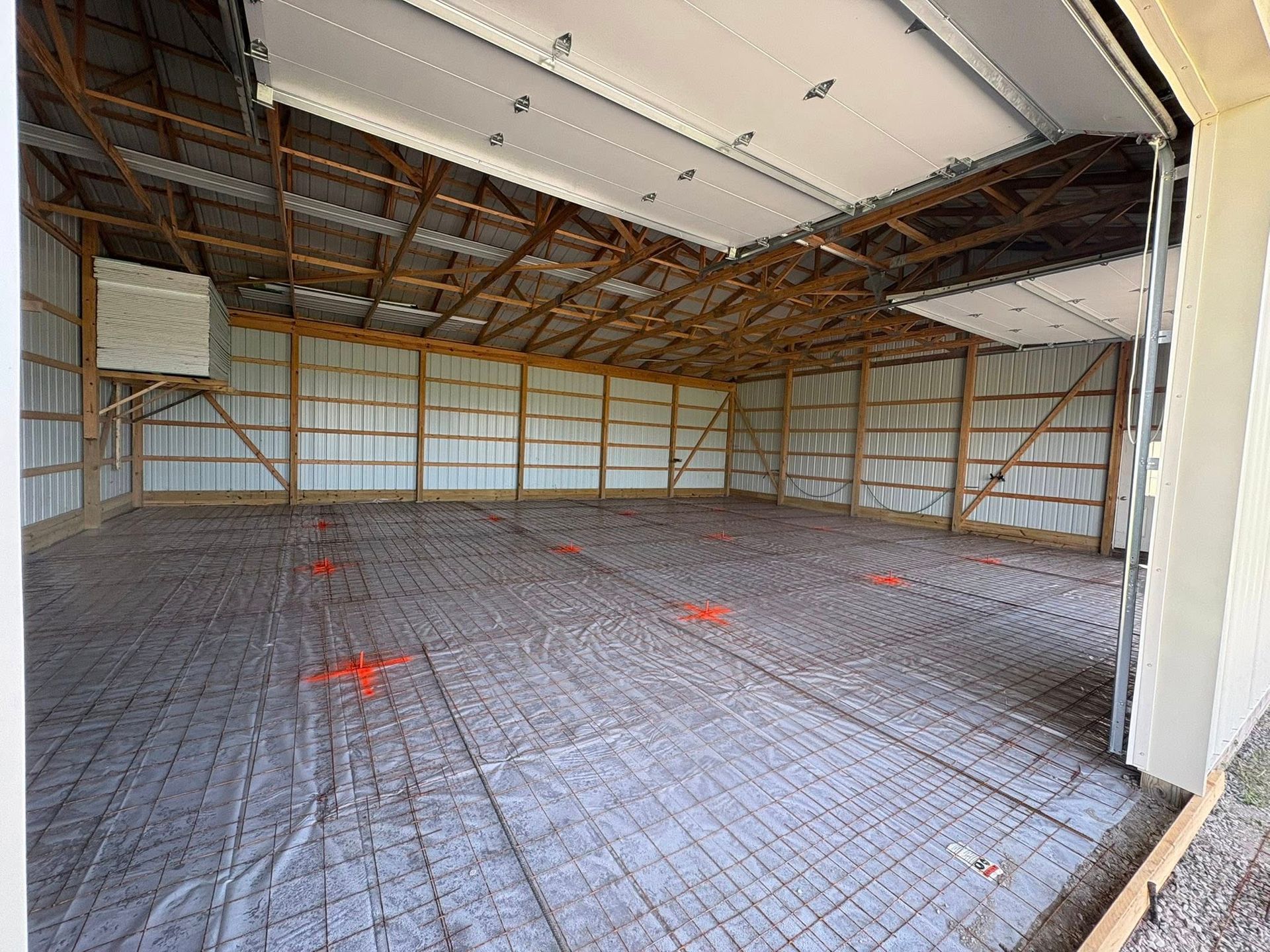 Interior of a large unfinished pole barn with a concrete floor prep area featuring wire mesh reinforcement.
