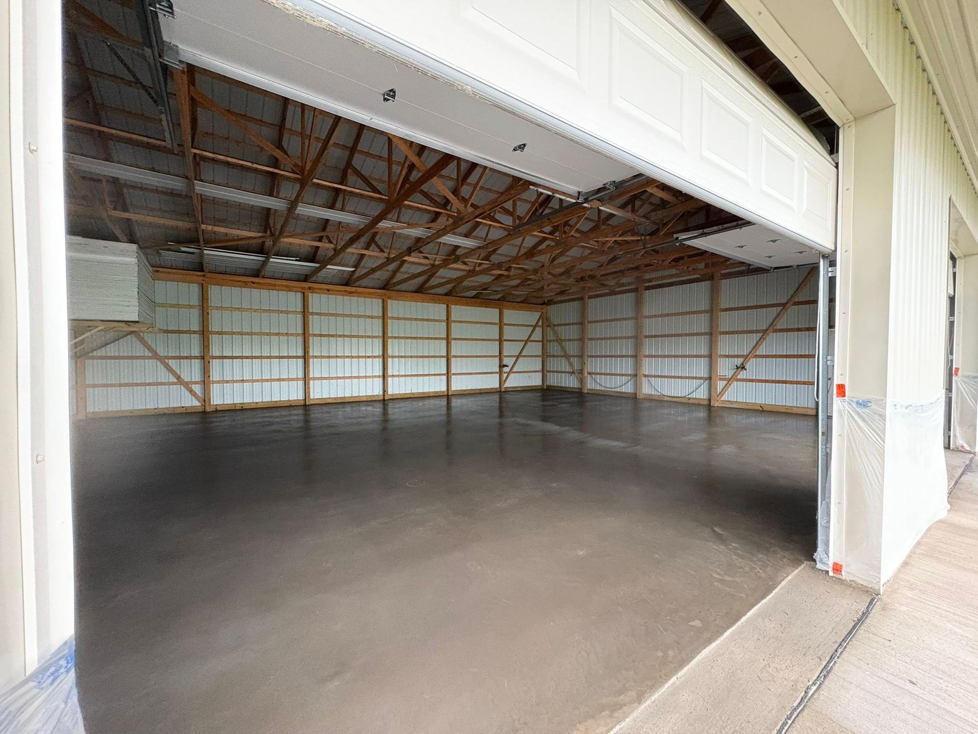 An empty, spacious garage with concrete floors, white metal walls, and exposed wooden ceiling trusses.