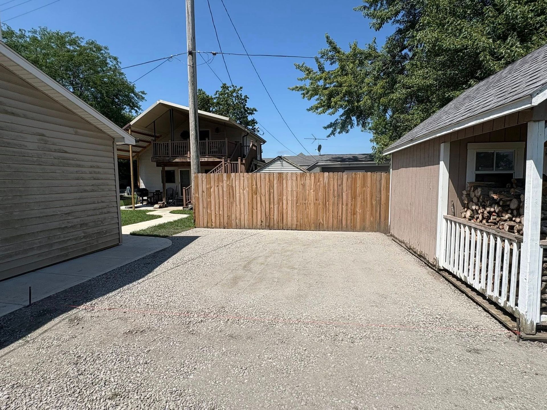 A gravel driveway between two buildings, leading to a wooden fence on a sunny day.