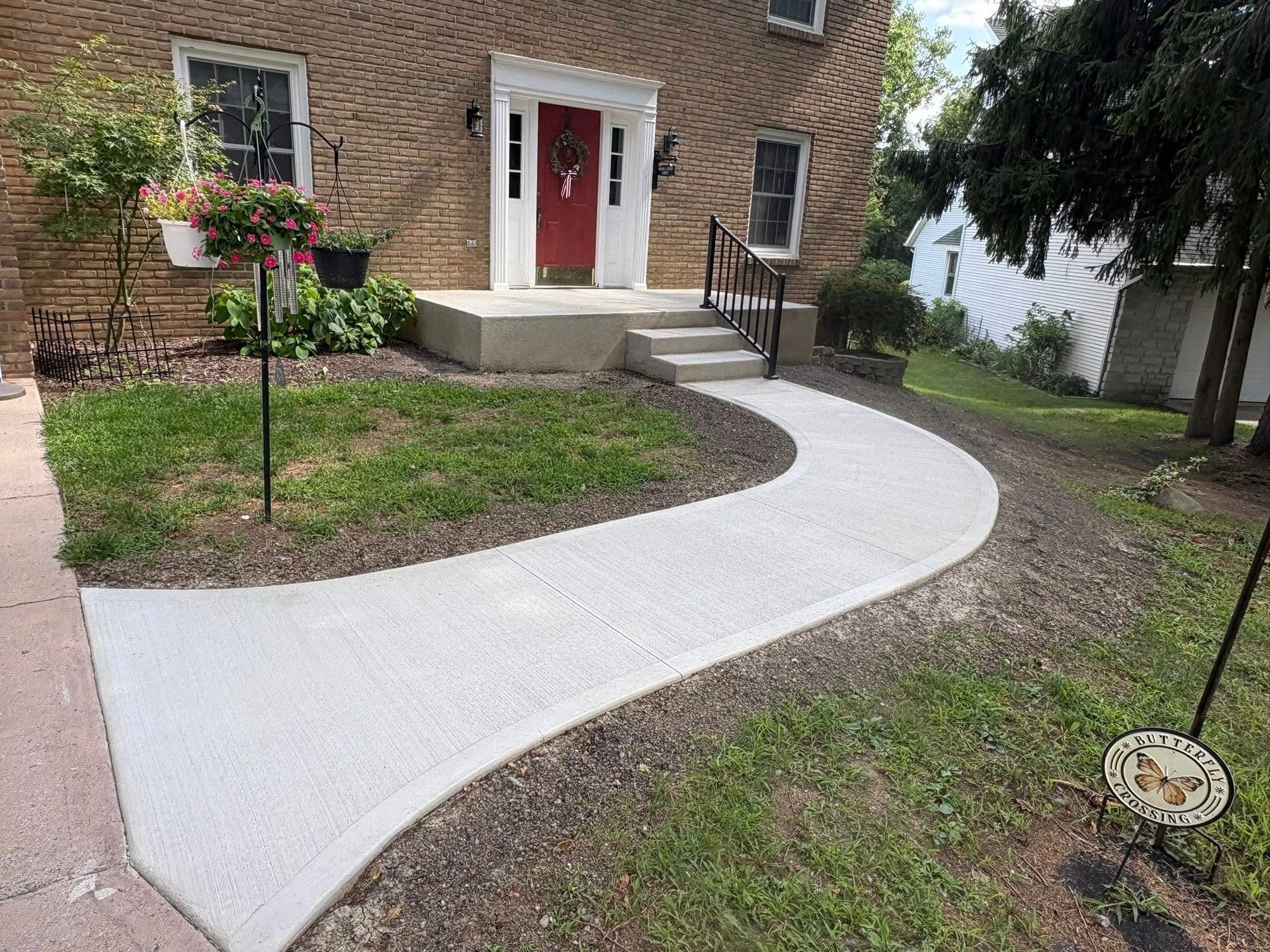 A wide, clean concrete walkway curves from the foreground toward the front door of a brick house with a white entryway.
