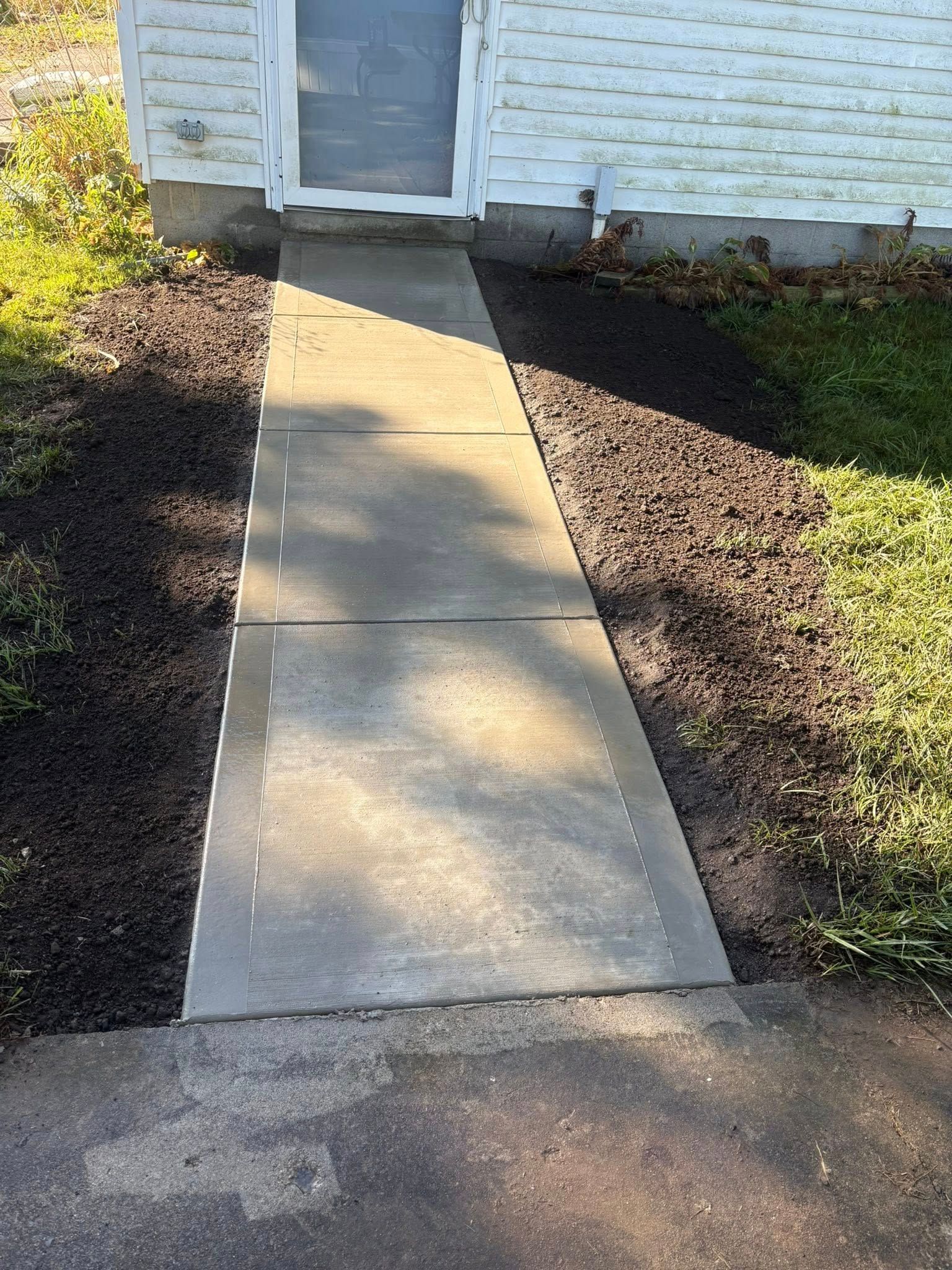 A concrete walkway leads from a paved driveway to a residential door surrounded by dark mulch.