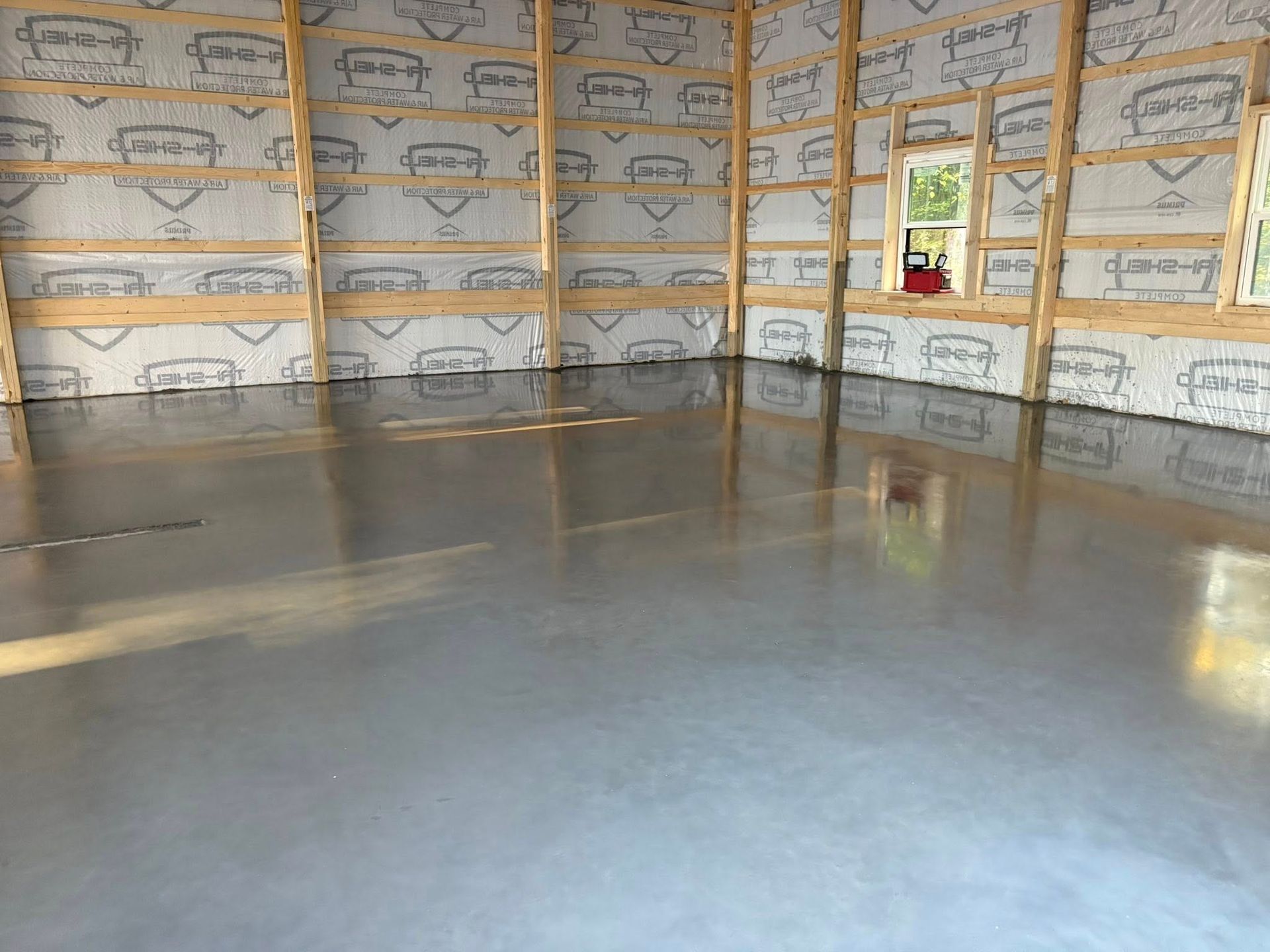 A smooth, polished gray concrete floor in an unfinished room with wooden wall framing and reflective wall insulation.