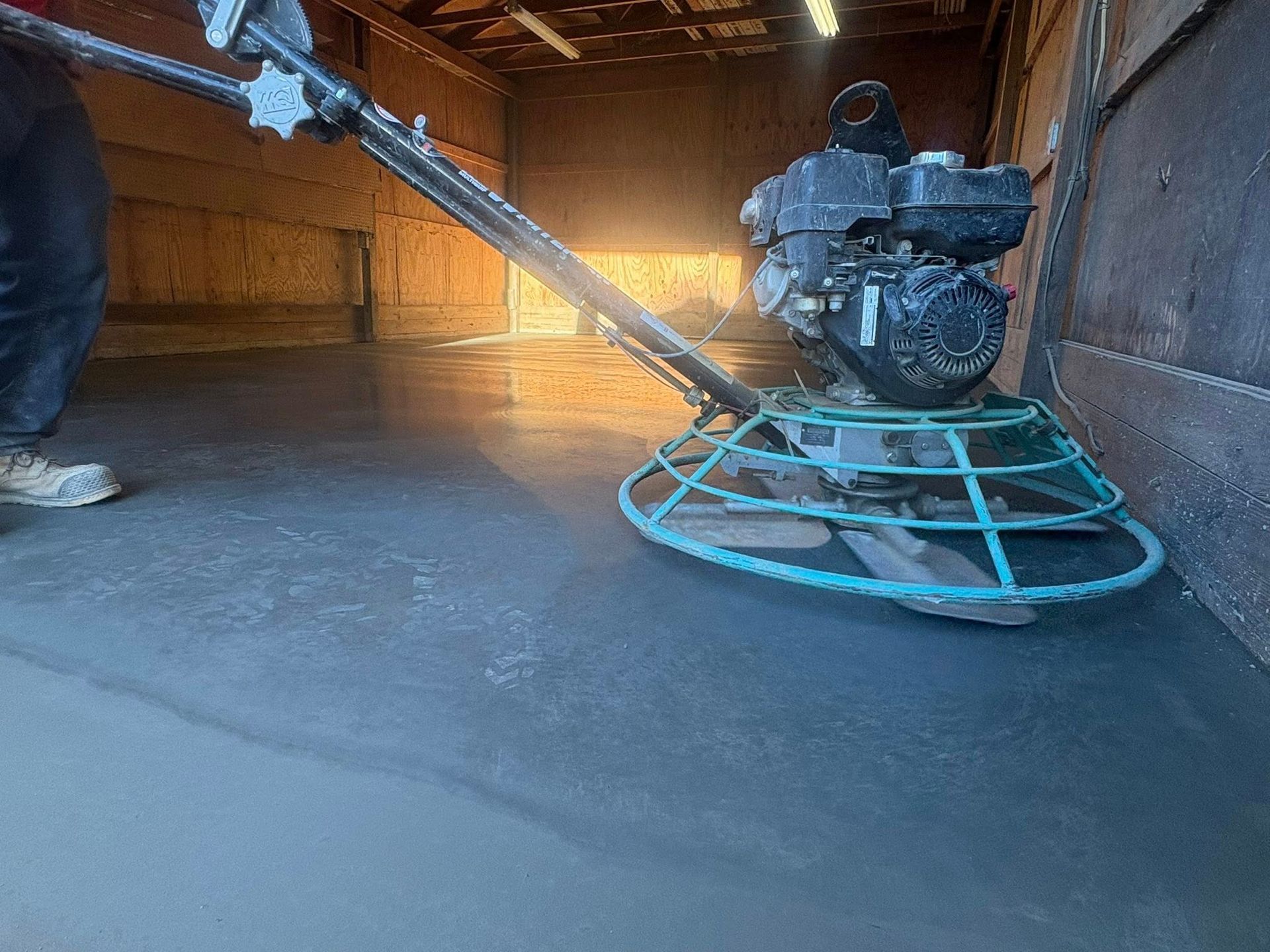A worker uses a power trowel to smooth wet concrete on the floor of an interior construction site.