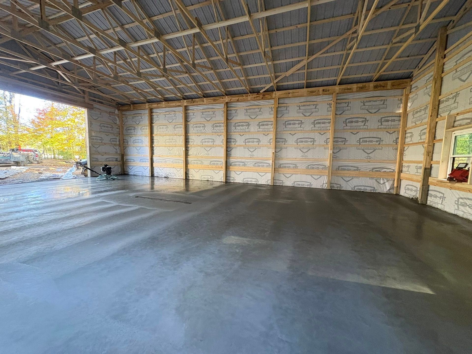 The interior of a large, unfinished post-frame building with a freshly poured concrete floor and insulated walls.