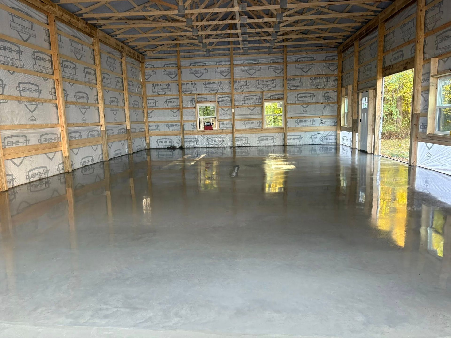Newly poured, smooth gray concrete floor inside an unfinished barn with exposed wood framing and windows.