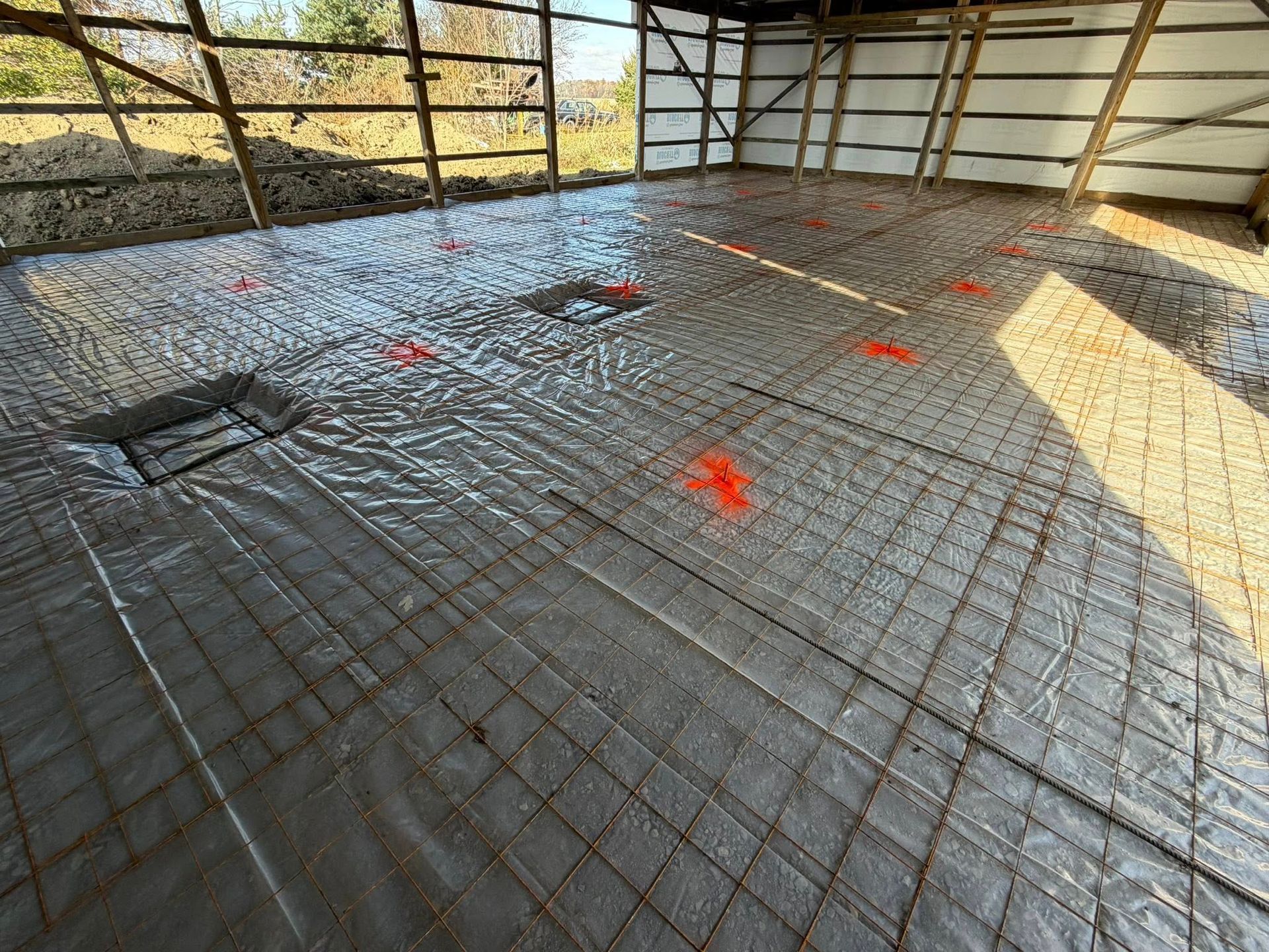 An interior construction site shows a vapor barrier over wire mesh, with bright orange markings on the floor.