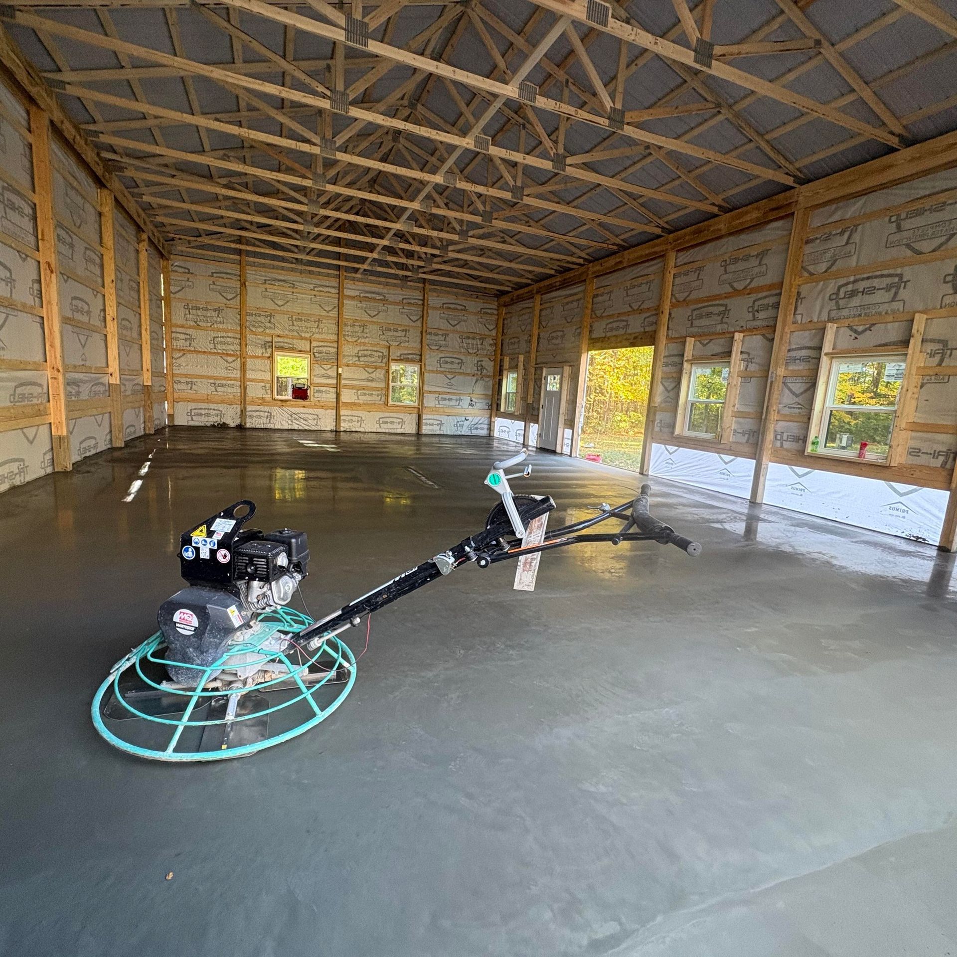 A power trowel sits on a smooth, freshly finished concrete floor inside an unfinished barn or metal building.