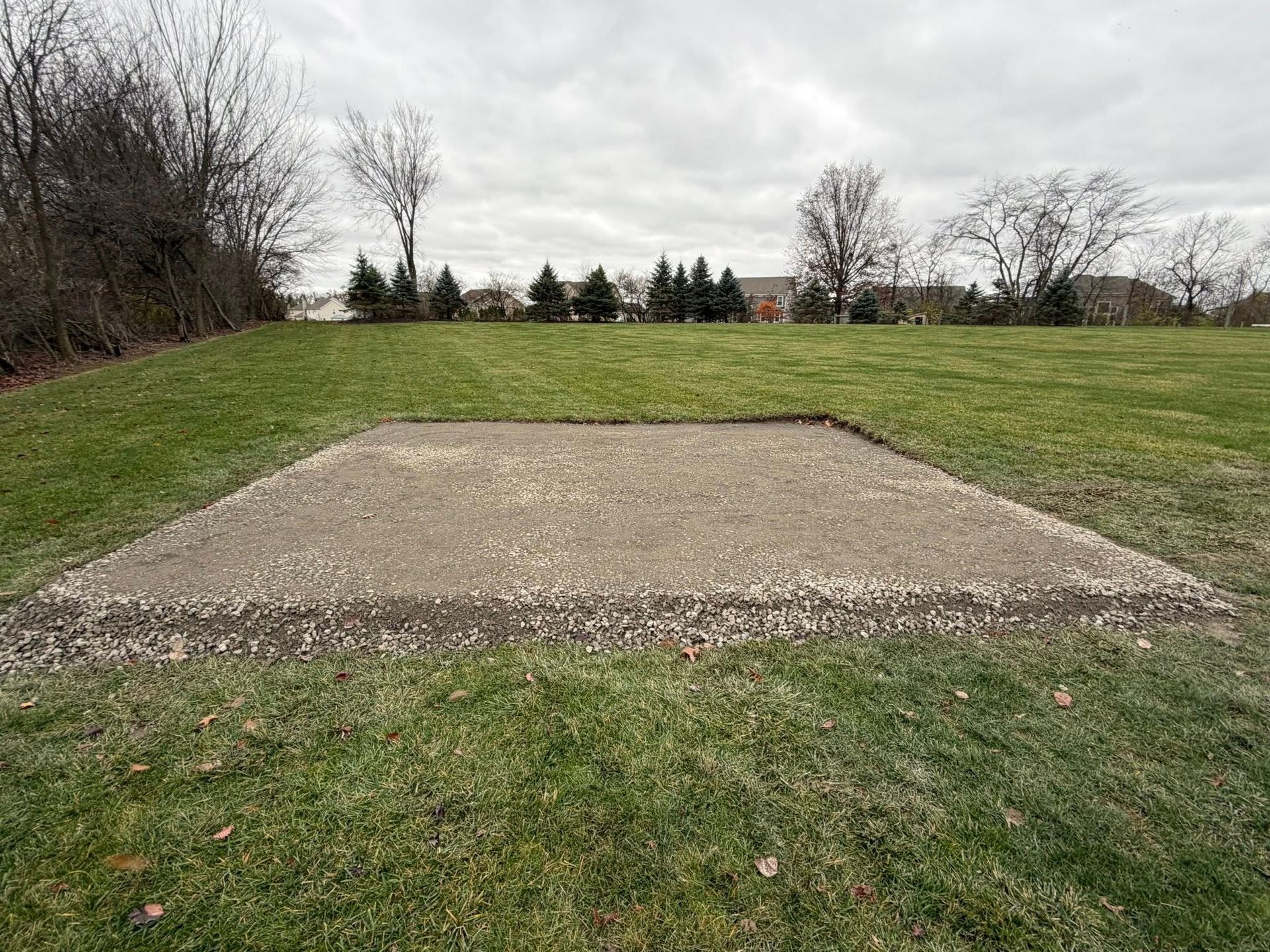 A rectangular concrete slab sits in the center of a grassy field under a cloudy, overcast sky.