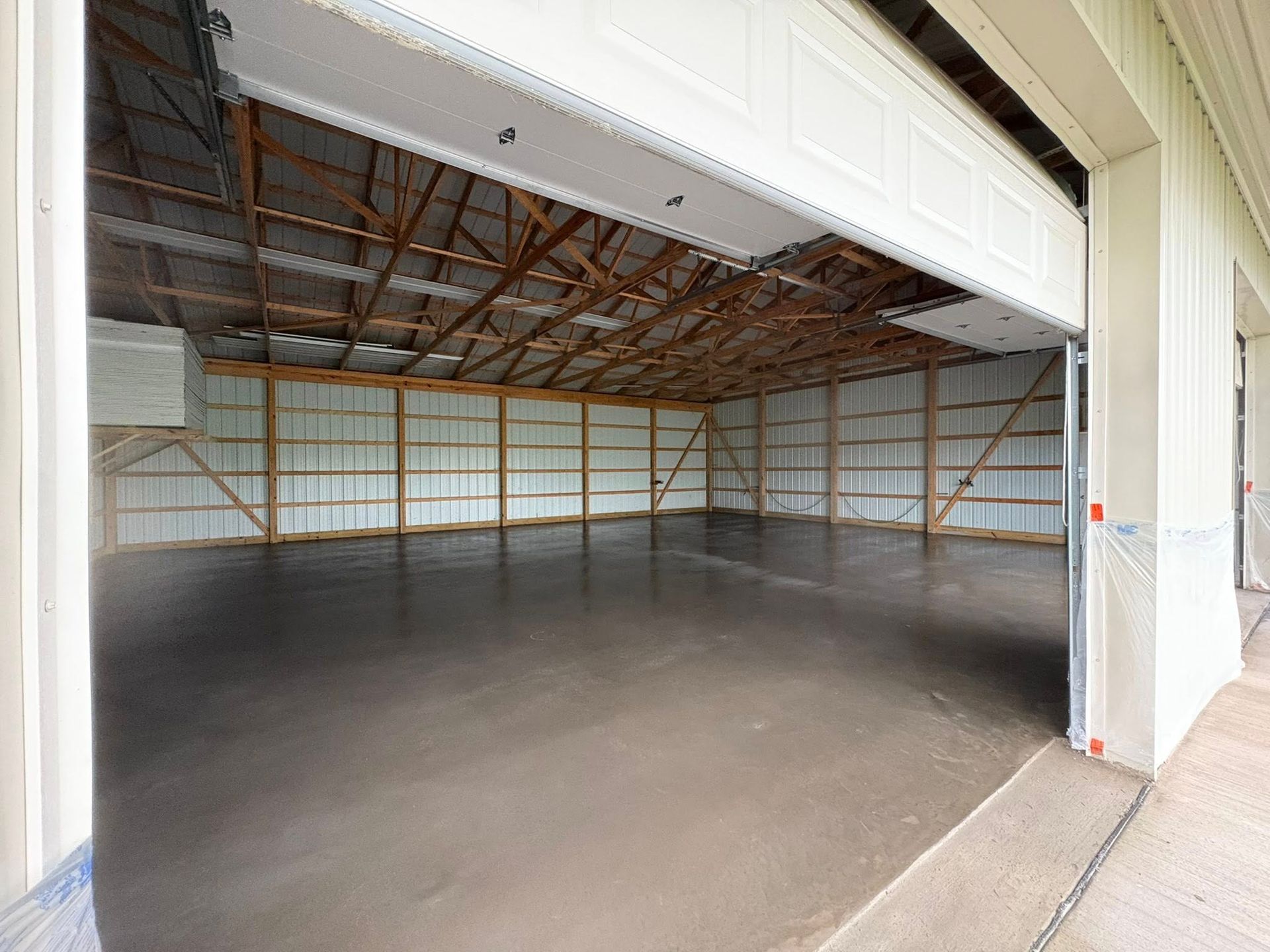 A view from outside looking into a large, empty pole barn with a concrete floor, wooden trusses, and a white metal interior.