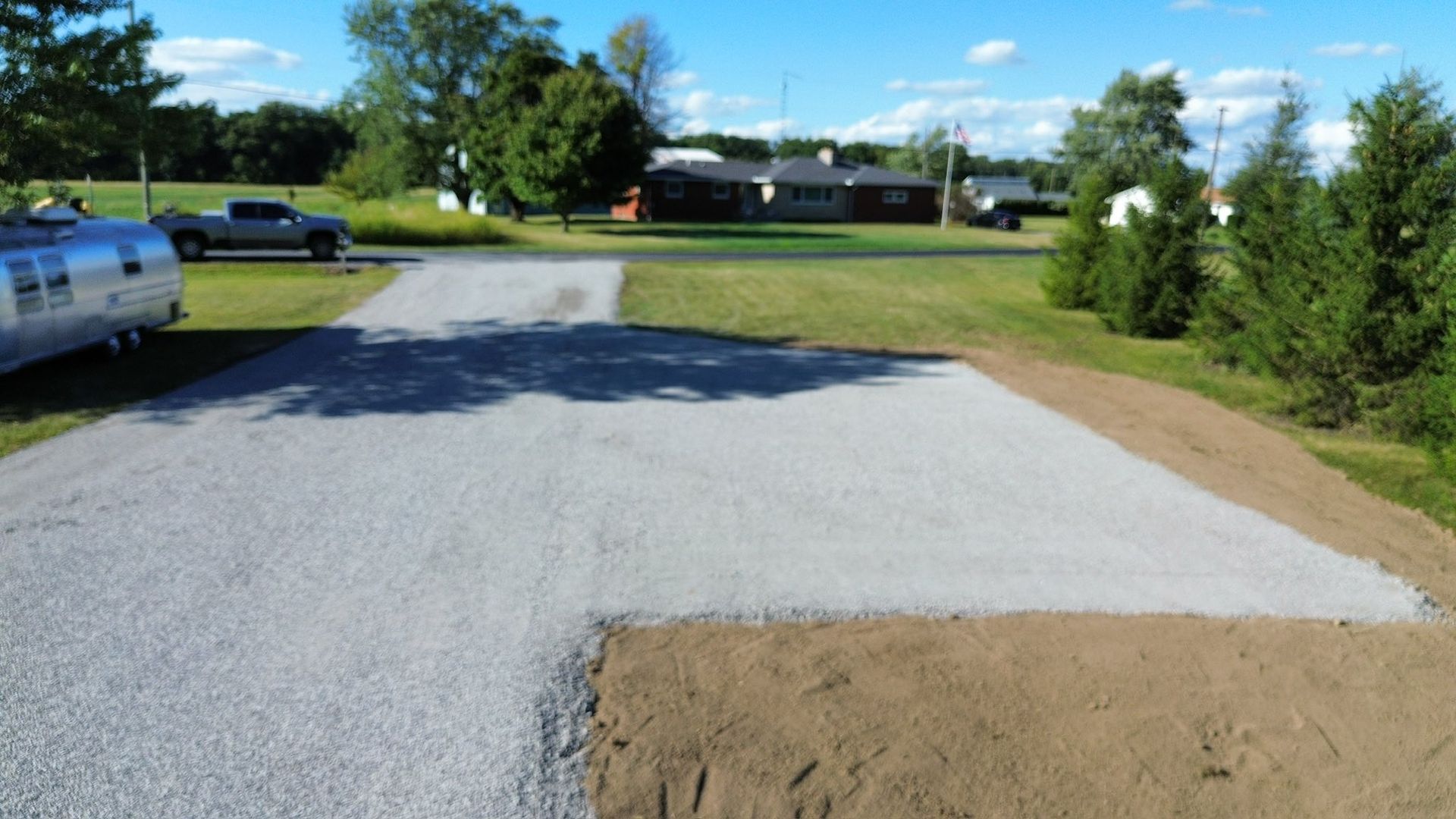 A fresh gravel driveway expansion with a light gray stone surface set against a grassy lawn and house under a blue sky.